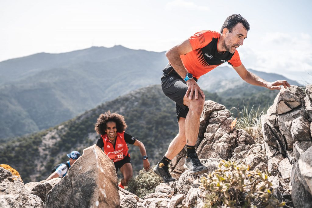 Skyrunners climbing rocky cliff face