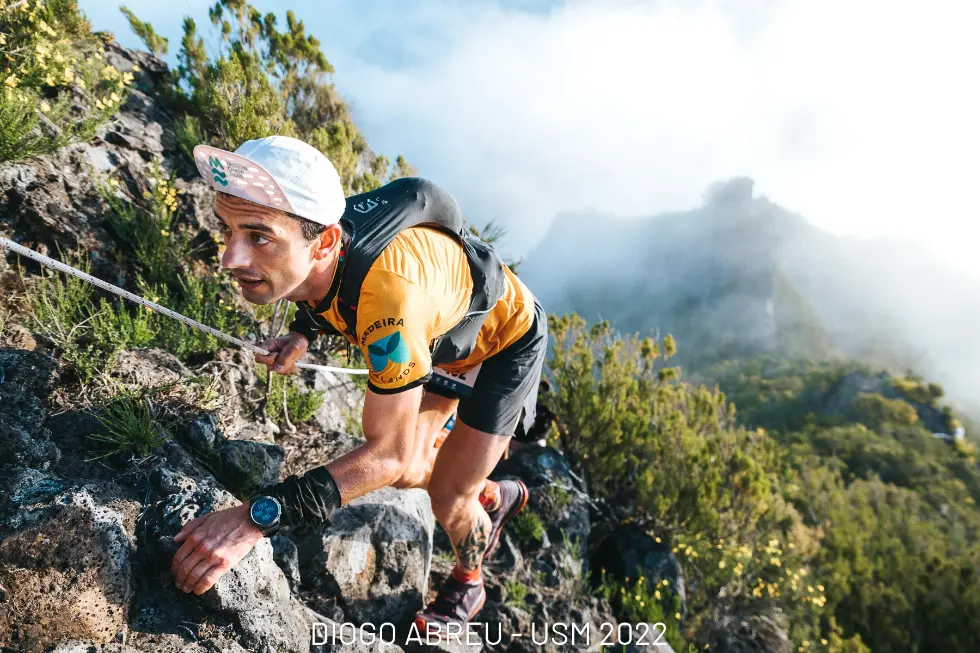 Male skyrunner up close holding rope as he goes up mountain