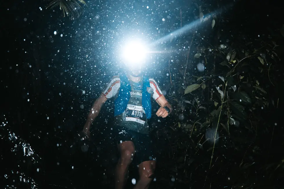 Male skyrunners running through tropical environment at night